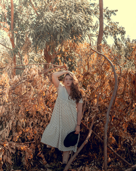woman in black and white polka dot dress standing near brown trees during daytime