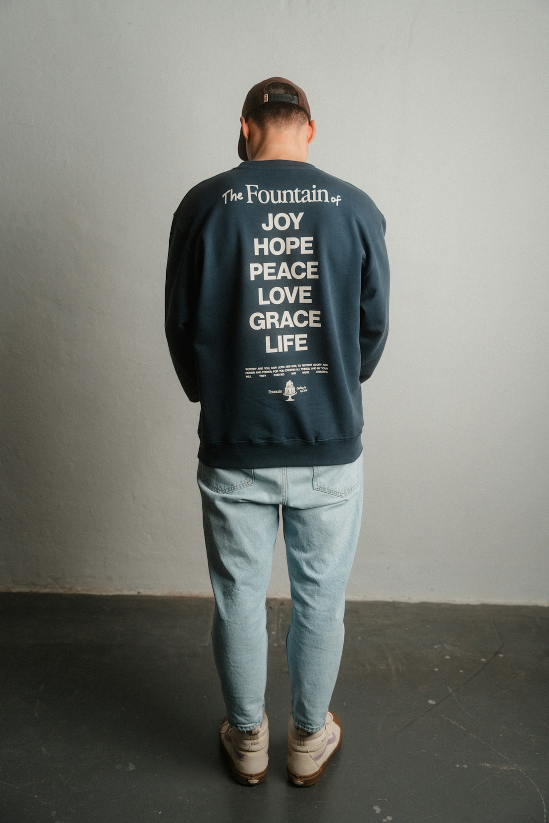 A man standing in front of a wall wearing a sweatshirt