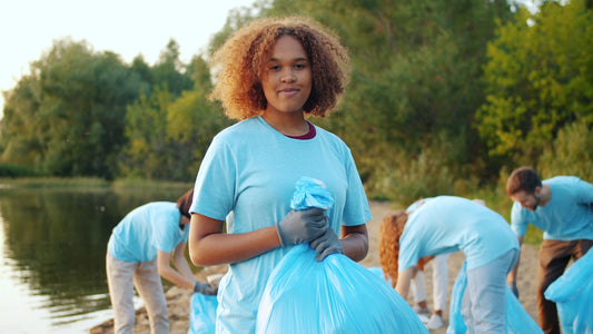 Young woman holding trash bag with volunteers cleaning beach
