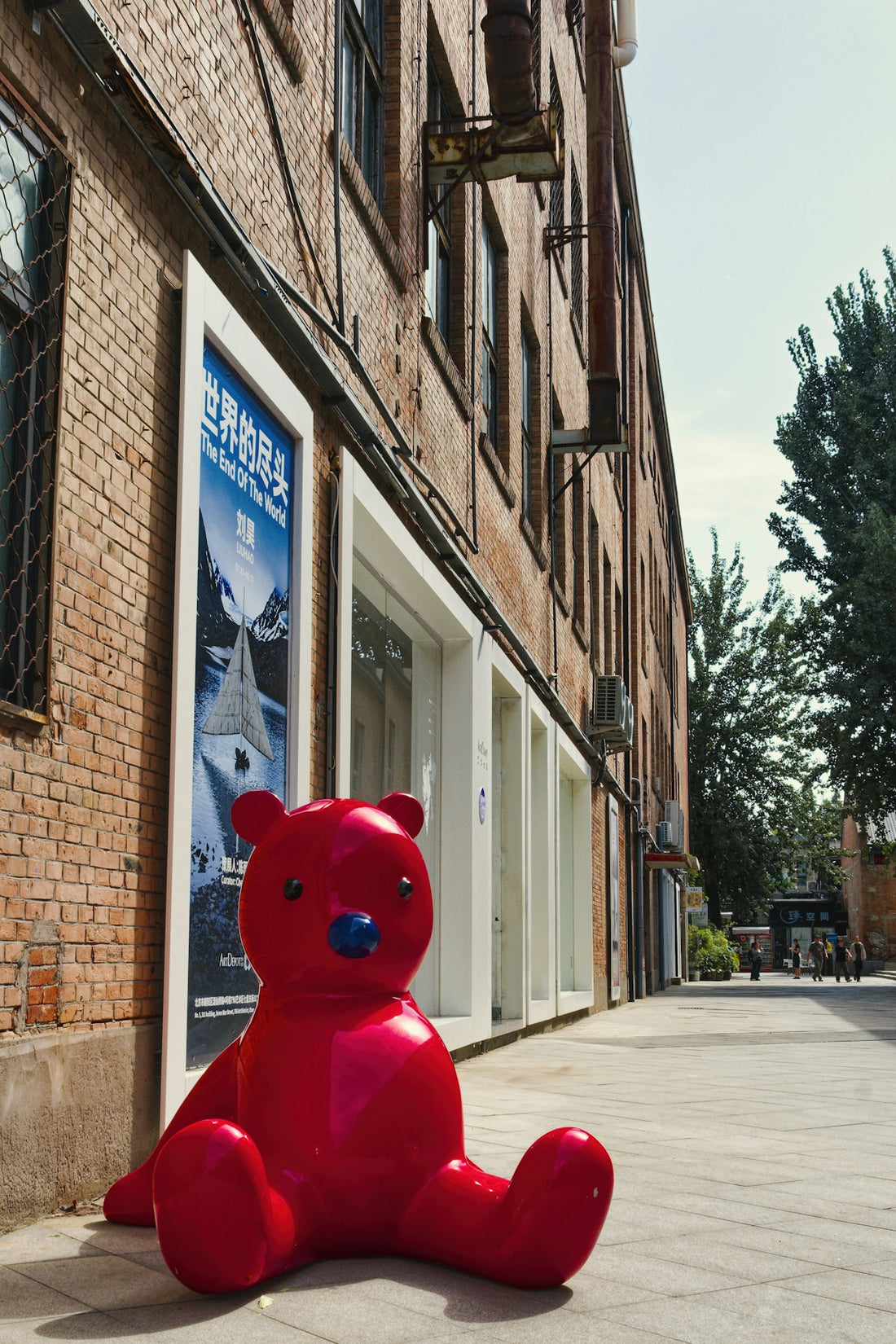 A large red teddy bear sculpture sits on sidewalk.